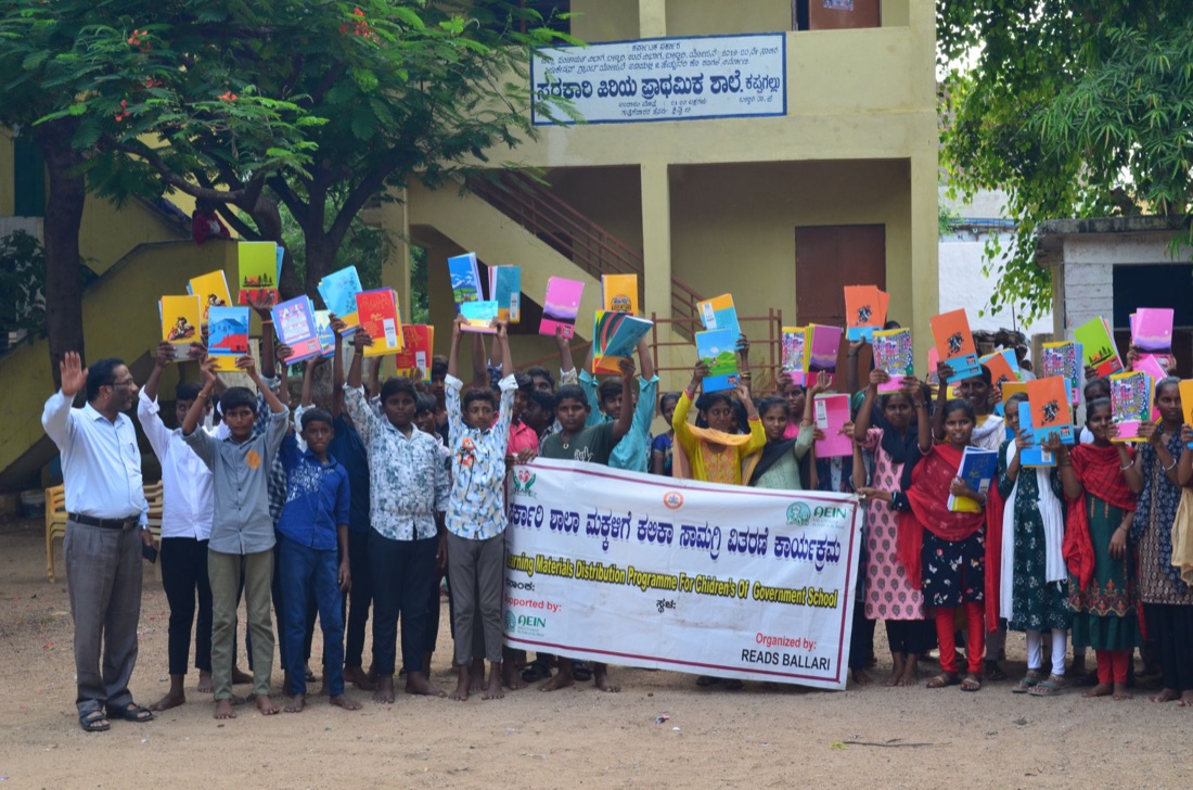 Children holding up notebooks and learning materials outside their school