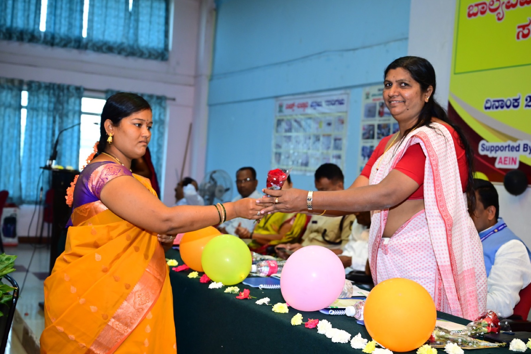 Two women exchanging a rose on stage at a community programme